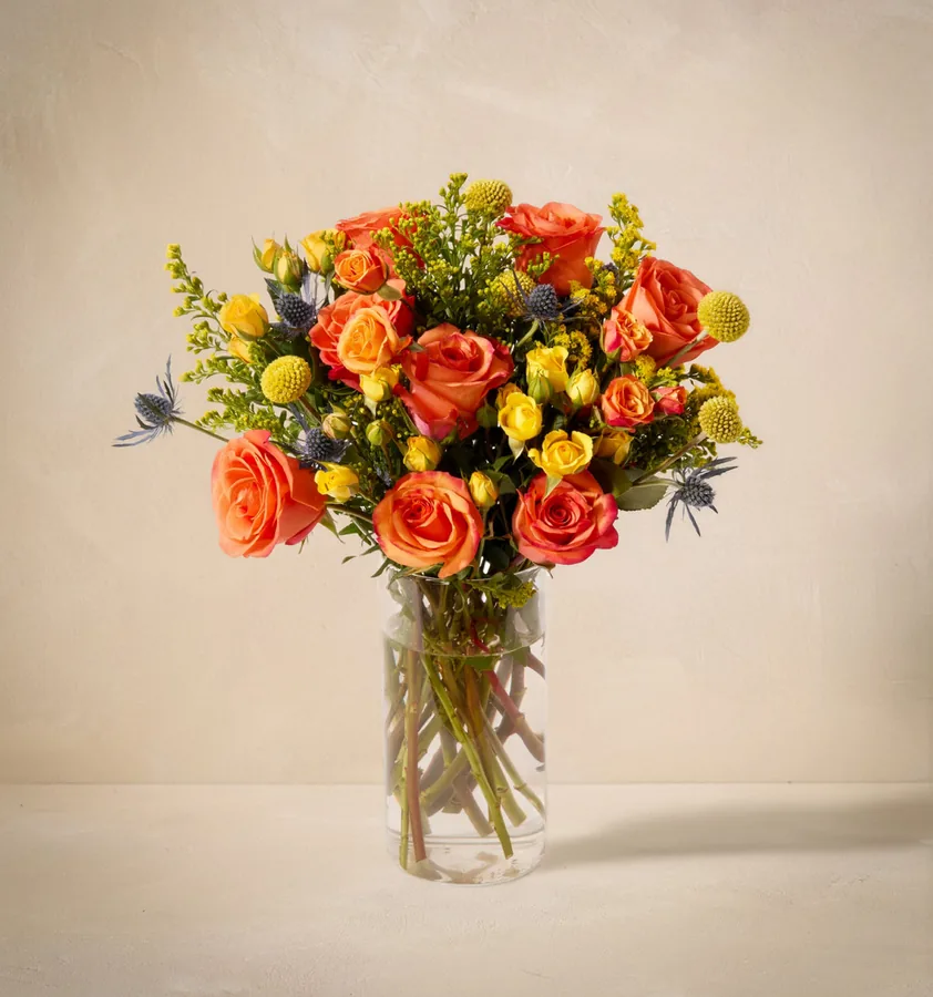 The Firecracker bouquet from UrbanStems with orange roses, blue thistle, and craspedia